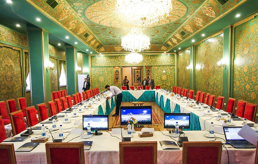 تالار زرین با میز کنفرانس U شکل، لپتاپها و دیوارهای سبز طلاکوب